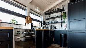 A modern kitchen with a stainless steel oven, black cabinets, and a wooden countertop. There is a window with a view of trees and a sign on the wall that reads "FOOD IS GOOD, WINE IS BETTER". - Paradise Cabin (Selfoss)