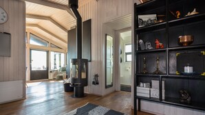 A modern living room with a wood-burning stove, a black shelving unit with decorative items, and a large window providing natural light. - Paradise Cabin (Selfoss)