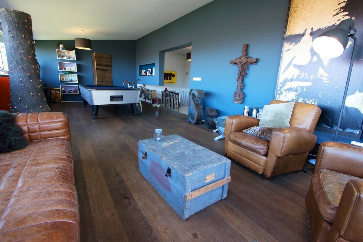 Ein Wohnzimmer mit Billardtisch, Ledersofas, einer blauen Kommode und einem Kruzifix an der Wand.