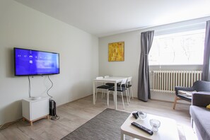 A modern living room with a flat-screen TV mounted on the wall, a dining table with chairs, a sofa, and a radiator. - Apartment R47 (Reykjavik)