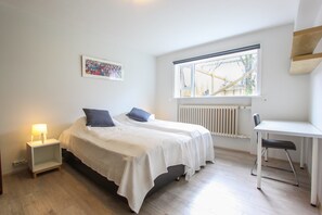 A bedroom with a bed, bedside table, chair, and a window with a view of a wooden structure outside. - Apartment R47 (Reykjavik)