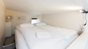 A single bed with white bedding, a bedside table with a lamp, and a wall-mounted fan. - Apartment SK2 (Reykjavik)