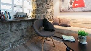 A cozy living area with a stone wall, a comfortable sofa, a modern chair, a coffee table with a book and a plant, and a bookshelf with books and a radio. - Apartment SK2 (Reykjavik)