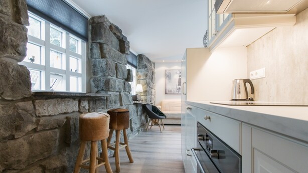 A kitchen with stone walls, wooden stools, and modern appliances. - Apartment SK2 (Reykjavik)