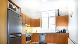 A modern kitchen with wooden cabinets, stainless steel appliances, and a window providing natural light. - Apartment Þ6 (Reykjavik)
