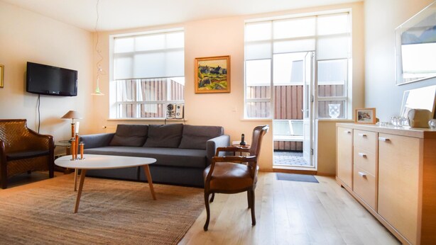 A living room with a sofa, chairs, a coffee table, a TV, and a painting on the wall. - Apartment Þ6 (Reykjavik)