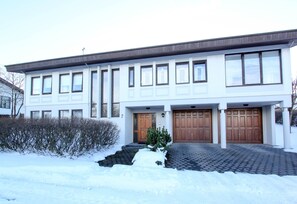 Uma casa moderna de dois andares com garagem, entrada coberta de neve e uma pequena área de jardim.