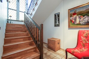 Uma escada de madeira com corrimão, uma cesta de vime, uma cadeira estofada vermelha e um quadro na parede.