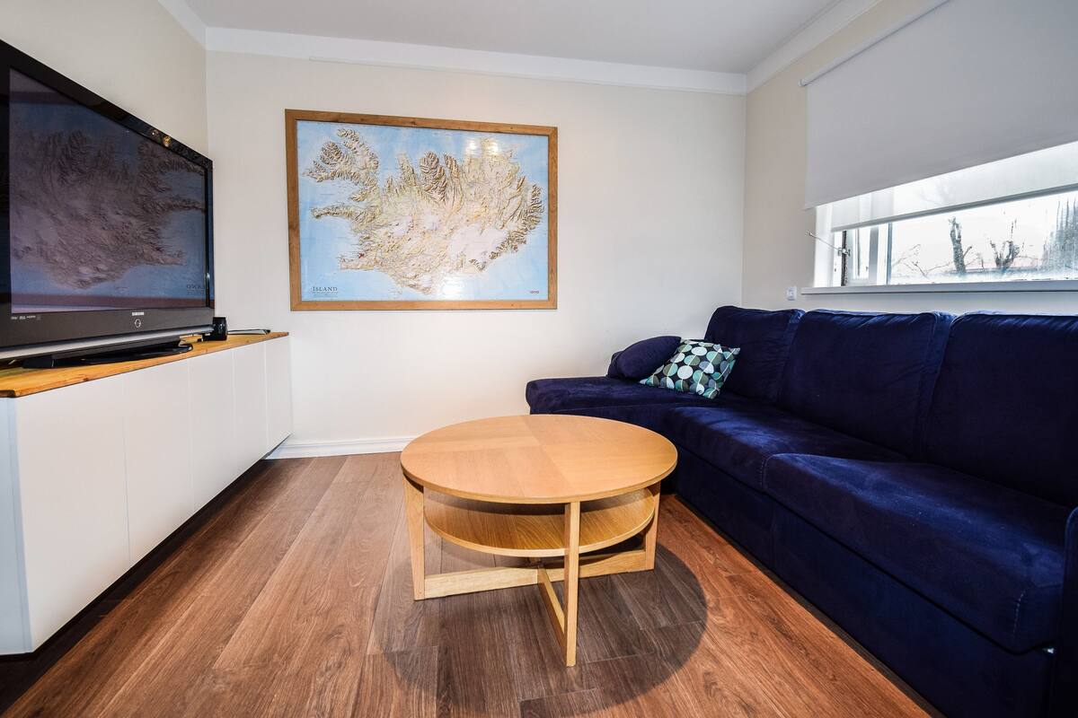 A living room with a TV, a round wooden coffee table, a dark blue sofa, and a framed map on the wall.