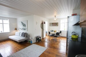 Een gezellige woonkamer met een bank, een eettafel met stoelen en een keukenhoek met een koelkast en waterkoker.