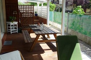 An outdoor patio with a wooden table and benches, surrounded by a white fence and greenery. - Chez Babeth (Toulouse)