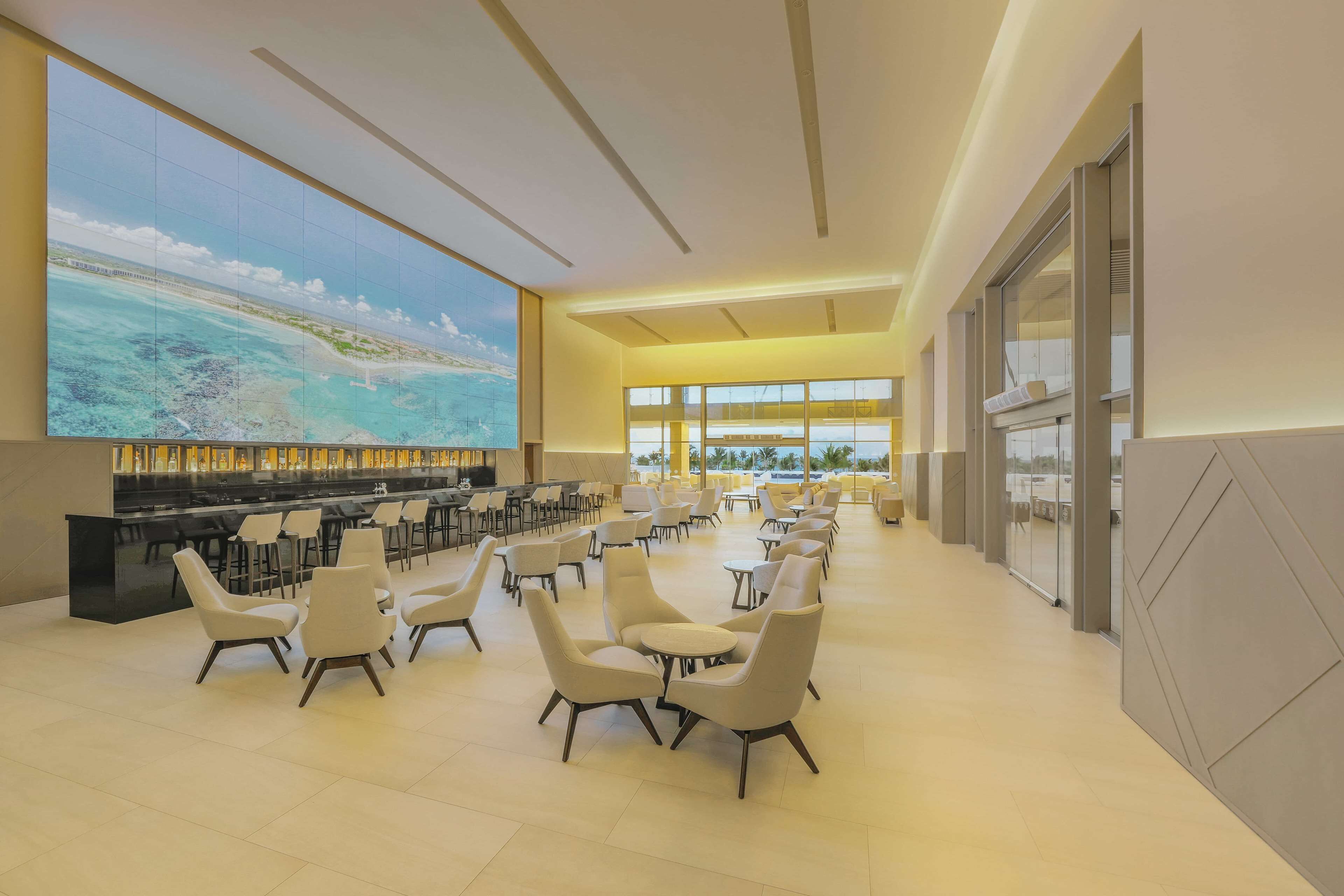 Amplia sala de estar con una pantalla grande que muestra una vista panorámica, asientos cómodos y una zona de bar.
