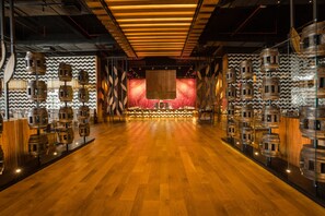 A spacious room with a wooden floor, a central stage, and walls adorned with cylindrical objects.