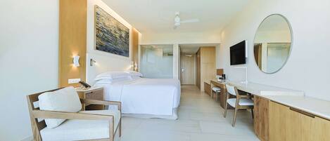 A modern hotel room with a bed, a desk, a chair, a large mirror, and a painting on the wall.