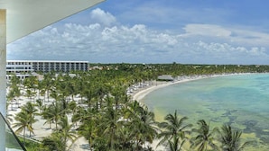 A balcony with a glass door, a seating area with chairs, and a view of a beach and ocean. - Barceló Maya Riviera - Adults Only - All Inclusive (Xpu-Ha)