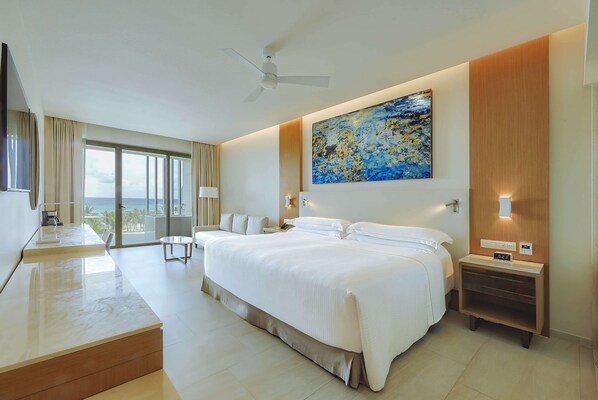 Een moderne hotelkamer met een groot bed, een plafondventilator, een schilderij en uitzicht op de oceaan.