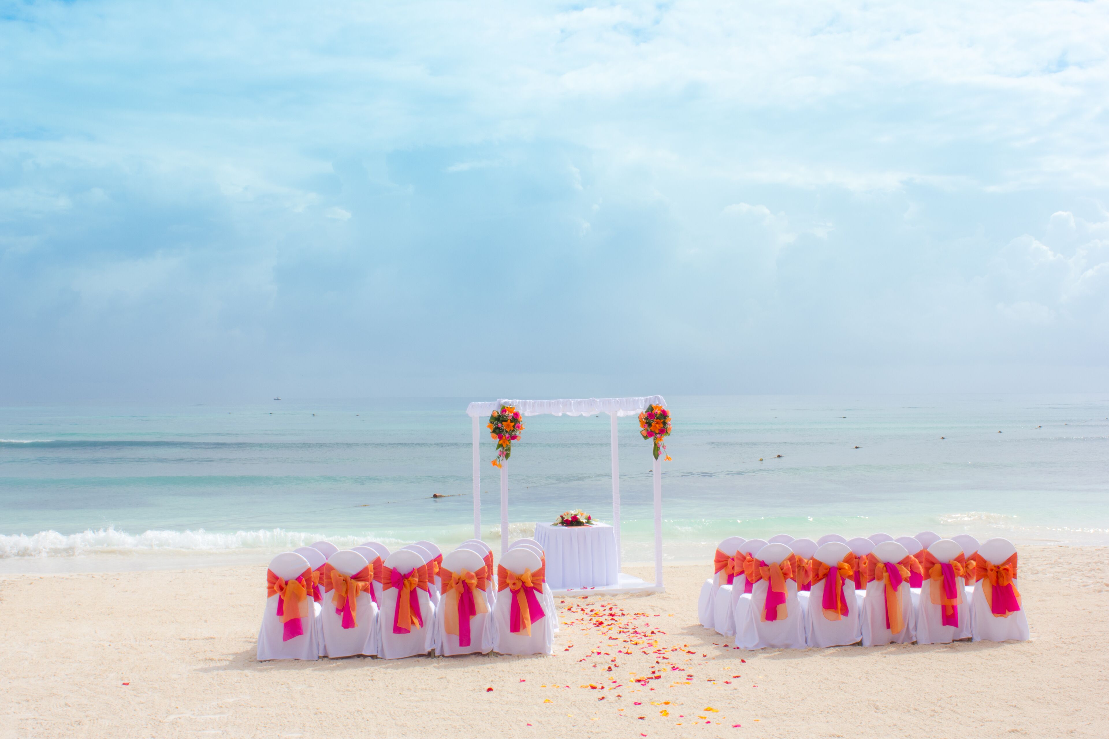 A beach wedding setup with white chairs and a white arch adorned with flowers.
