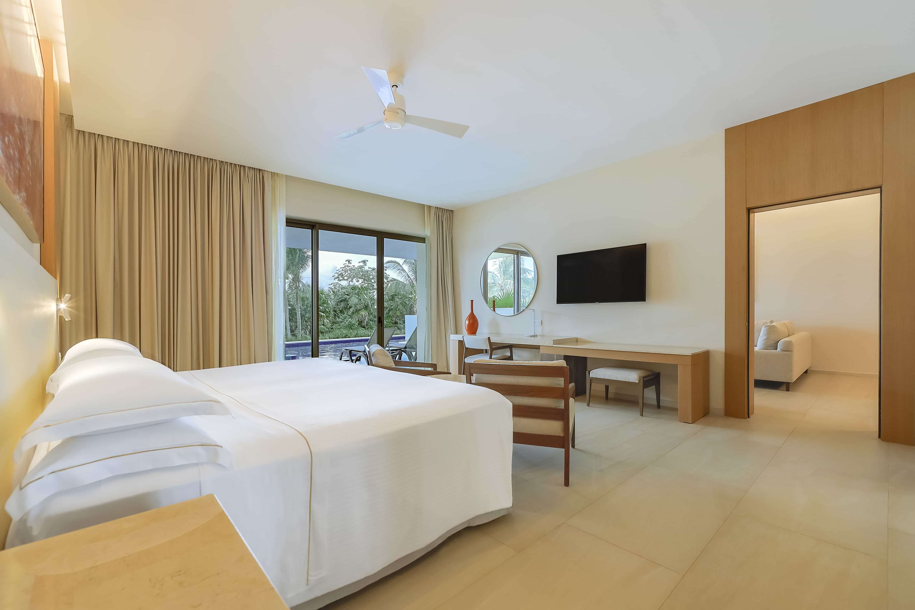 Habitación de hotel con cama, escritorio, silla, televisión y vistas al exterior.
