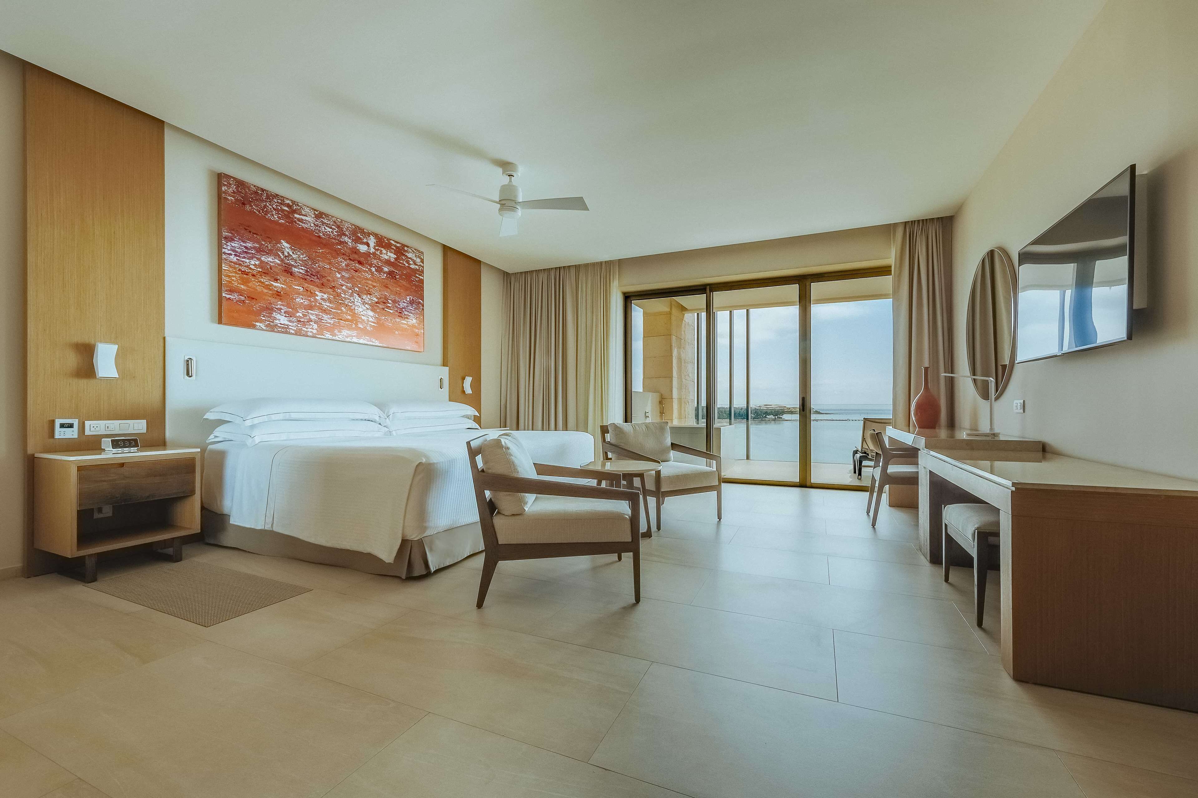 Habitación de hotel con cama, escritorio, silla y un amplio ventanal con vistas.