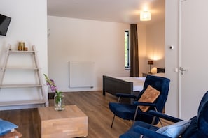 A modern room with a bed, a desk, a chair, a small table, a radiator, a TV, and a window with curtains. - Peace, space and comfort in ParelDuyn, situated between the village of Oostkapelle and the beach. (Oostkapelle)