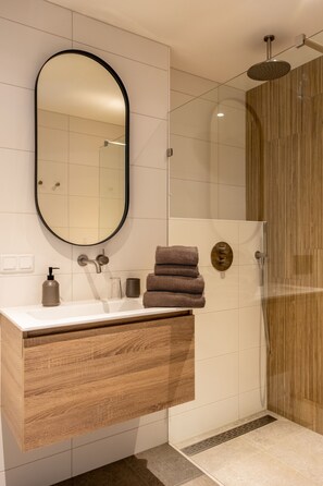 A modern bathroom with a wooden vanity, a large mirror, a shower with a glass door, and a towel rack.