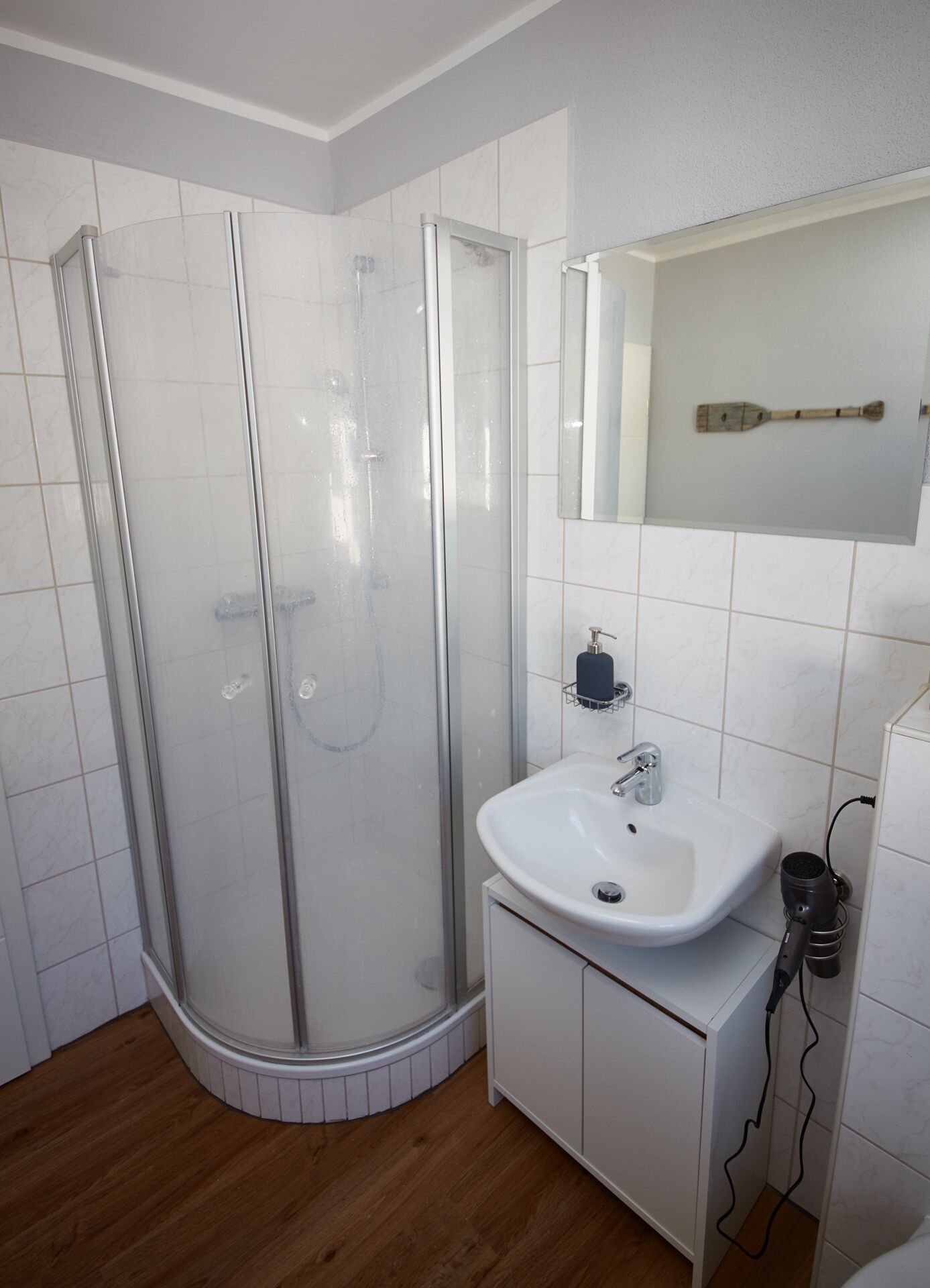 Un baño moderno con ducha de vidrio, un lavamanos blanco y un espejo encima.