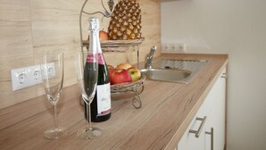 A kitchen counter with a wine bottle, two glasses, a pineapple, and a basket of apples. - Holiday home Eifelträume for 6 people (Birresborn)