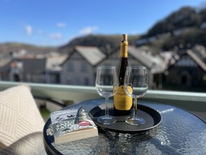 A table with a bottle of wine, two glasses, and a book titled "The Salt Path" on a glass table with a view of houses in the background. - Southcliffe Bed & Breakfast (Lynton)