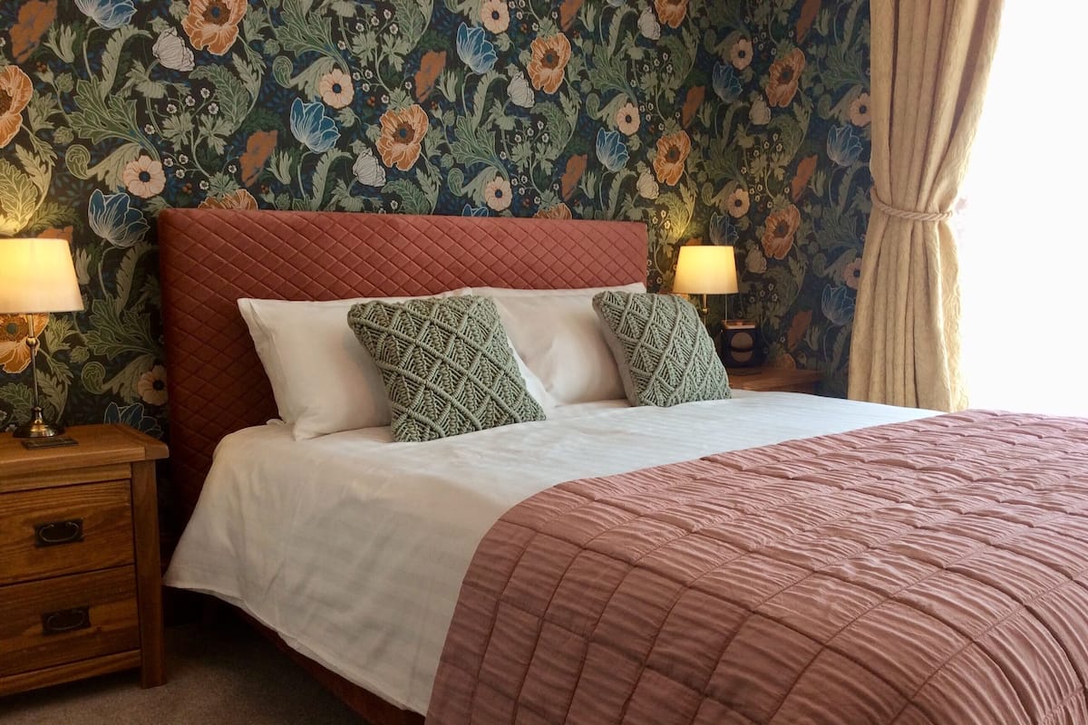 A neatly made bed with a quilted headboard, two pillows, and a bedside table with lamps.