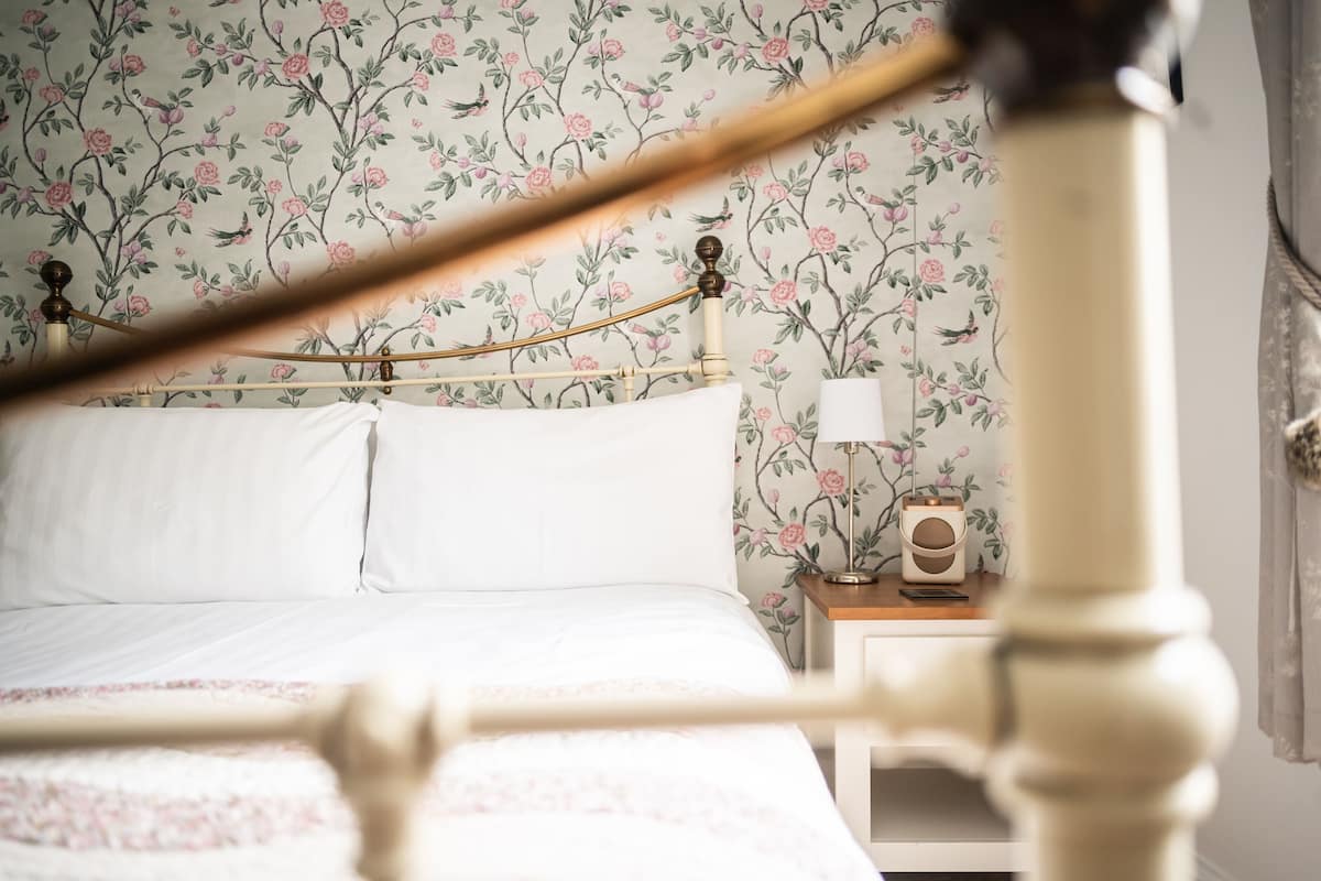 A bed with white linens, a nightstand with a lamp, and a floral wallpaper pattern.