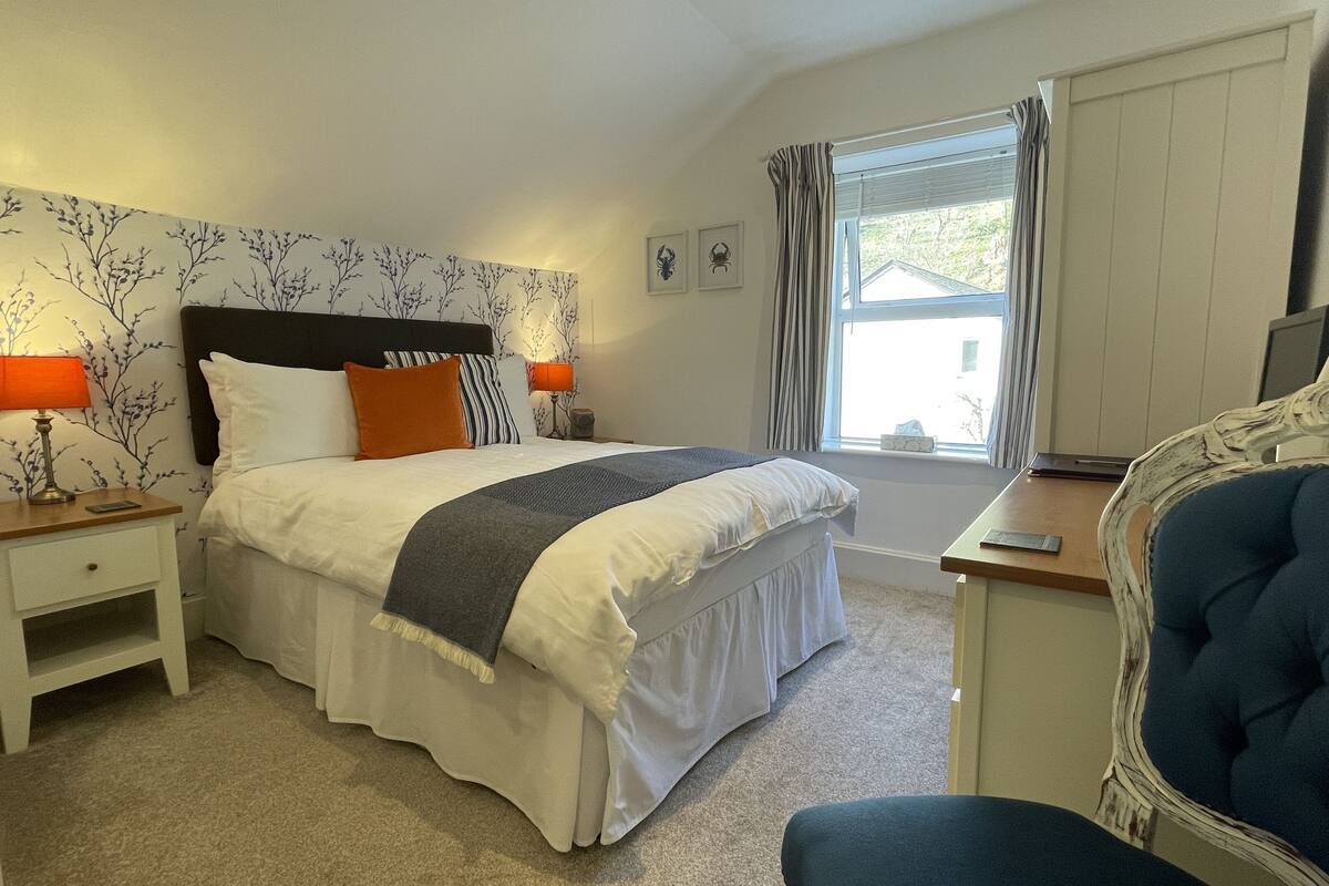 A bedroom with a bed, nightstands, a desk, a chair, and a window with curtains.