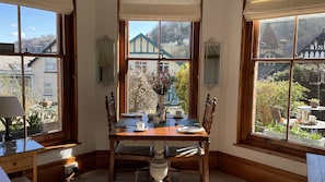 Enjoy a meal for two at this cozy corner room's dining table, with a view of a traditional building and a hill in the background.