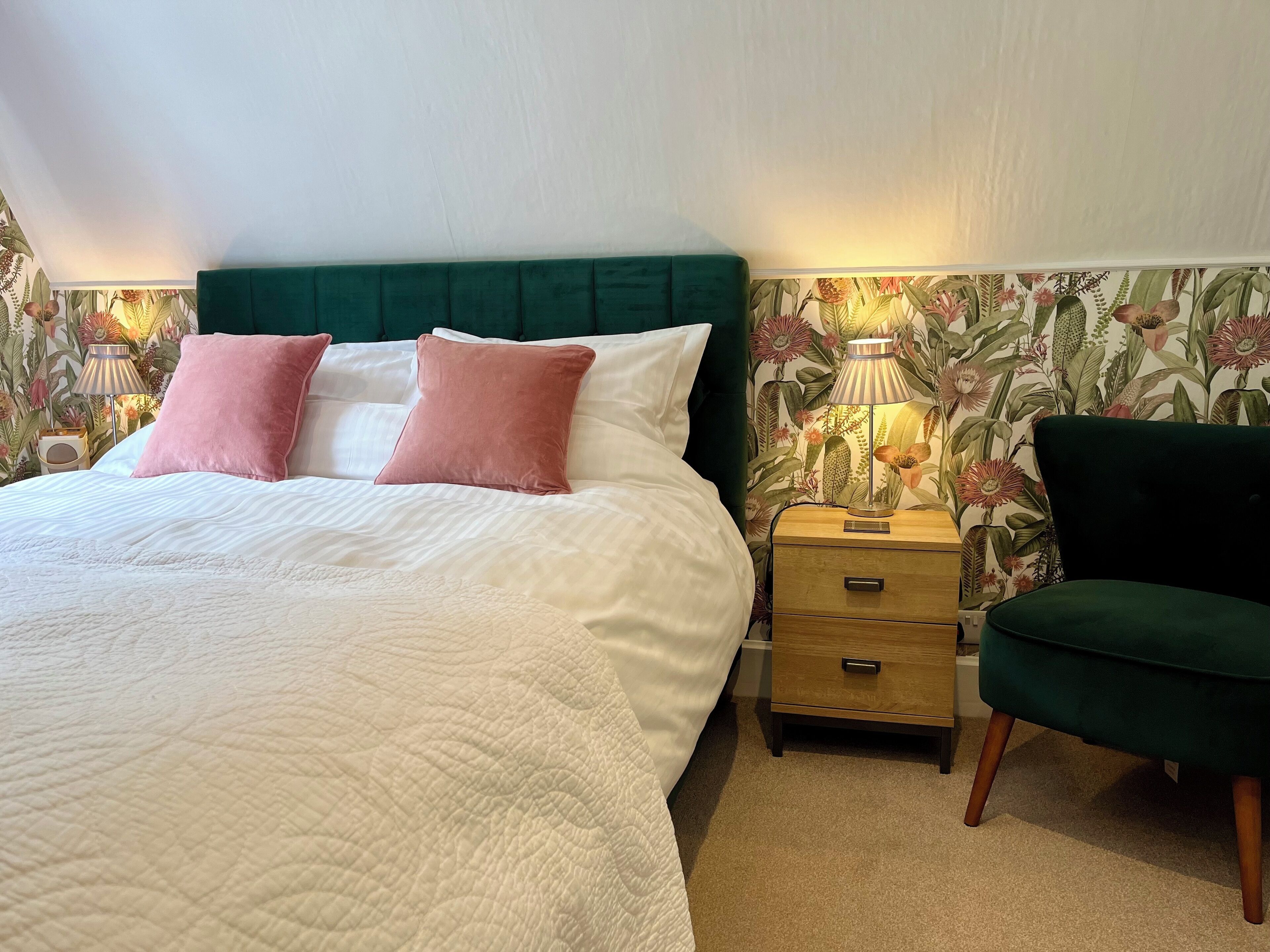 A neatly made bed with a green headboard, two pink pillows, and a bedside table with a lamp.