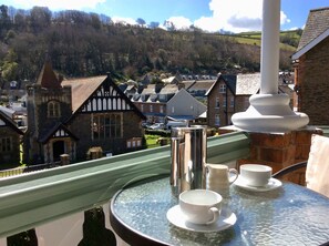 A balcony with a table set for tea, overlooking a village with traditional buildings and a hill in the background. - Southcliffe Bed & Breakfast (Lynton)