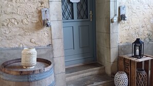 Un muro de piedra, un barril de madera, una puerta azul con un letrero que dice 'BIENVENUE' y un farol sobre una pequeña mesa.