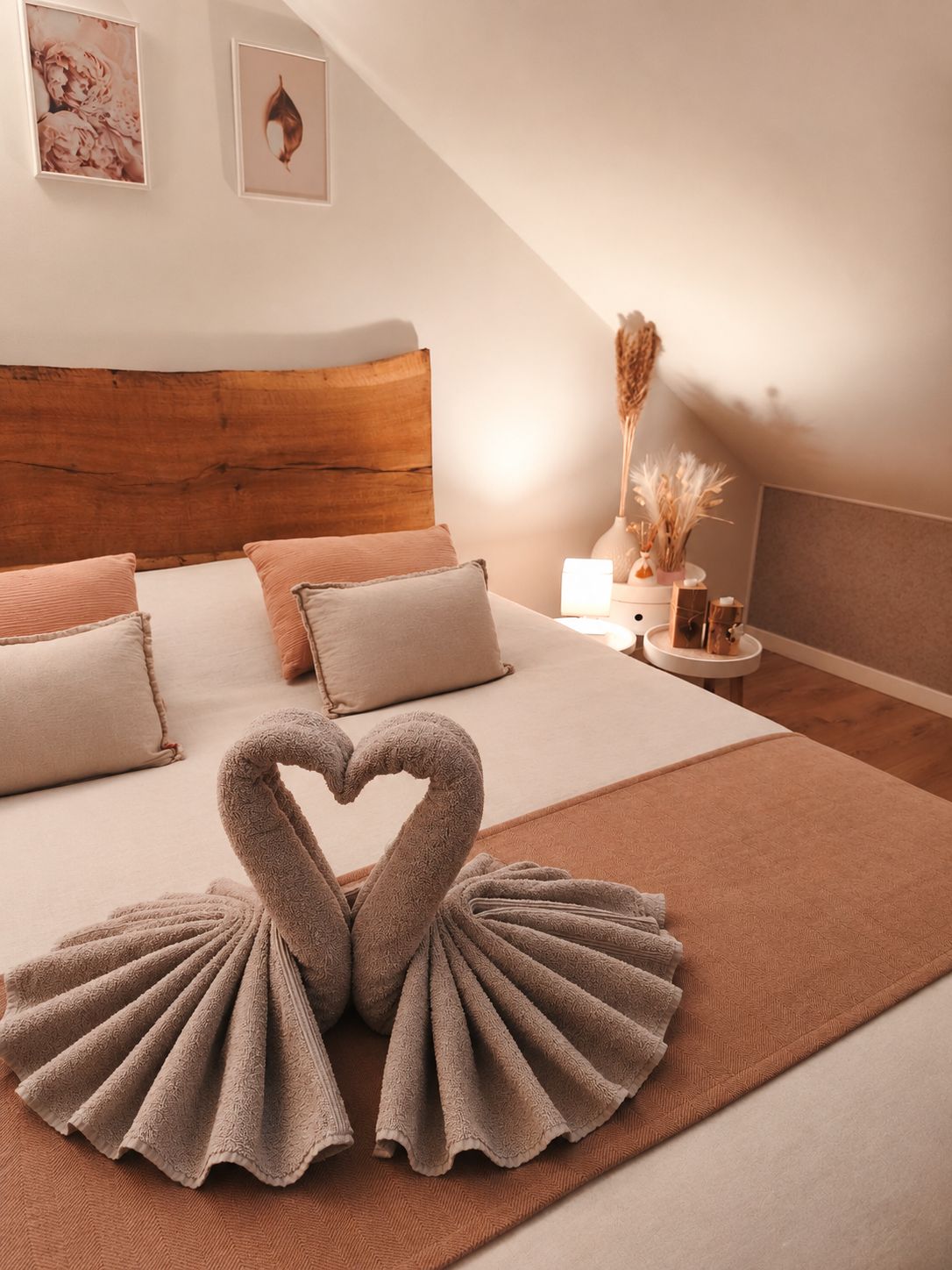 Un dormitorio con cabecera de madera, una cama con ropa de cama color beige y un arreglo de toallas con forma de corazón en el suelo.