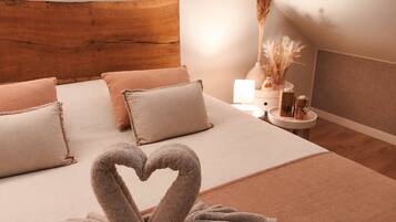 Un dormitorio con cabecera de madera, una cama con ropa de cama color beige y un arreglo de toallas con forma de corazón en el suelo.