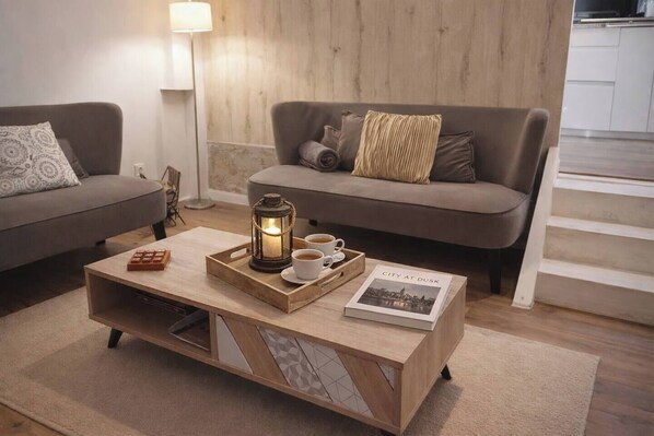 Un salón acogedor con una mesita de madera, un farol, dos tazas de café y un libro titulado 'City at Dusk'.