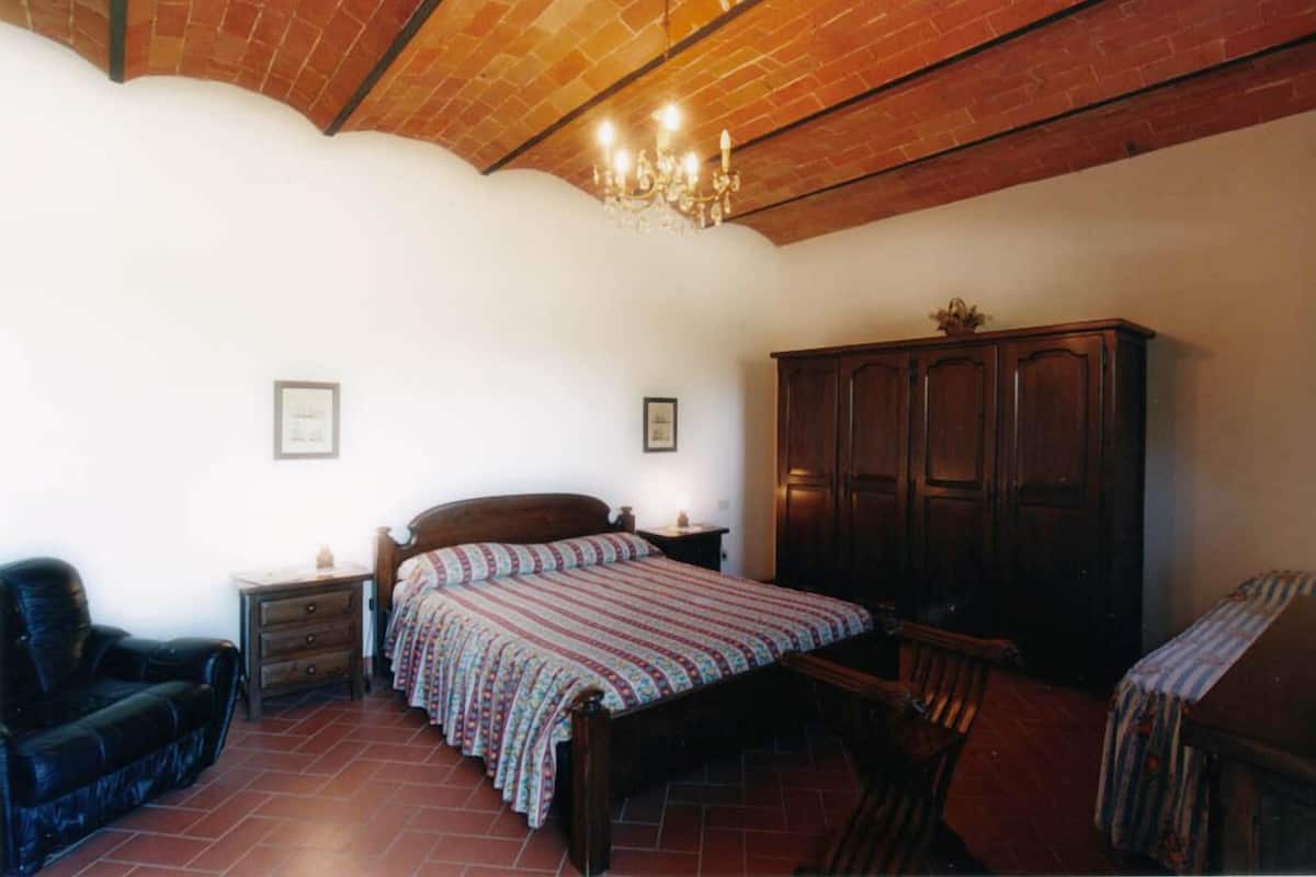 Un dormitorio con una cama de madera, una silla, un armario y una araña.