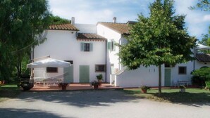 A white building with a tiled roof, a covered outdoor seating area, and potted plants. - Podere Castagno (Lorenzana)