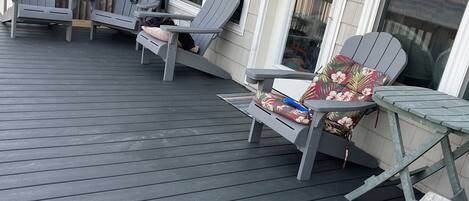 Een terras met Adirondack stoelen en een tafel, houten omheining en een gebouw met grote ramen.