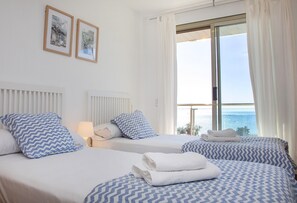 Camera d'albergo con due letti, biancheria bianca e vista sul mare.
