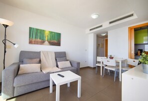 Un soggiorno con divano, tavolino, un quadro, una lampada e un angolo cottura con tavolo e sedie.