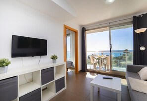 Un soggiorno moderno con una televisione a schermo piatto, un tavolino console bianco, un divano grigio e un balcone con tavolo e sedie.