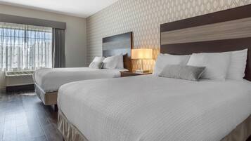 A hotel room with two beds, a large window with curtains, a patterned wallpaper, and a modern headboard.