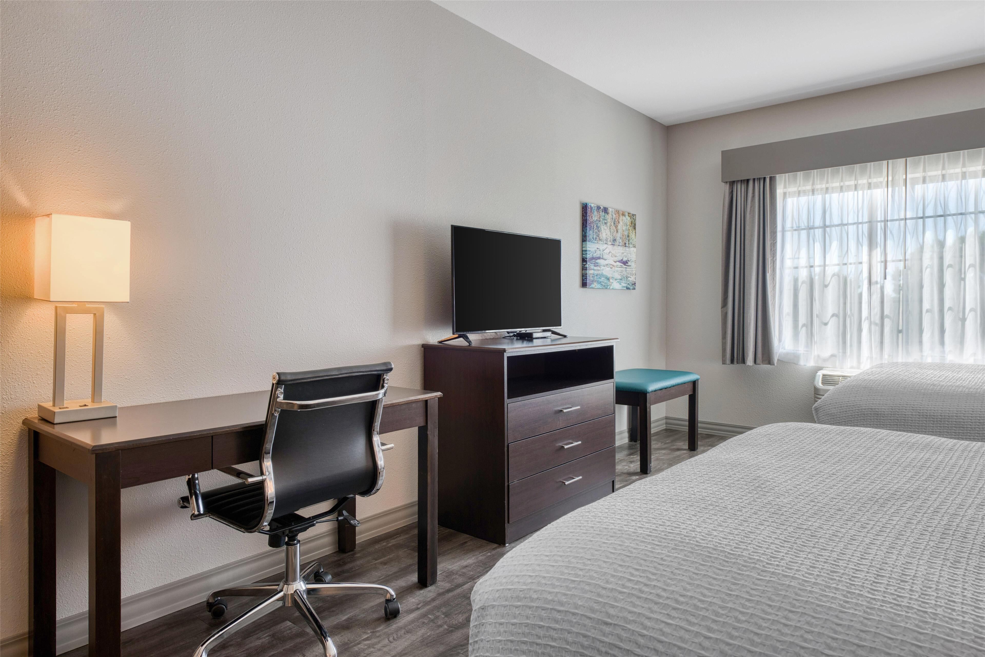 A hotel room with a desk, chair, television, and two beds.