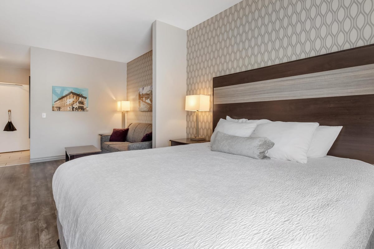 A modern hotel room with a large bed, two bedside tables, a chair, and a patterned wall.