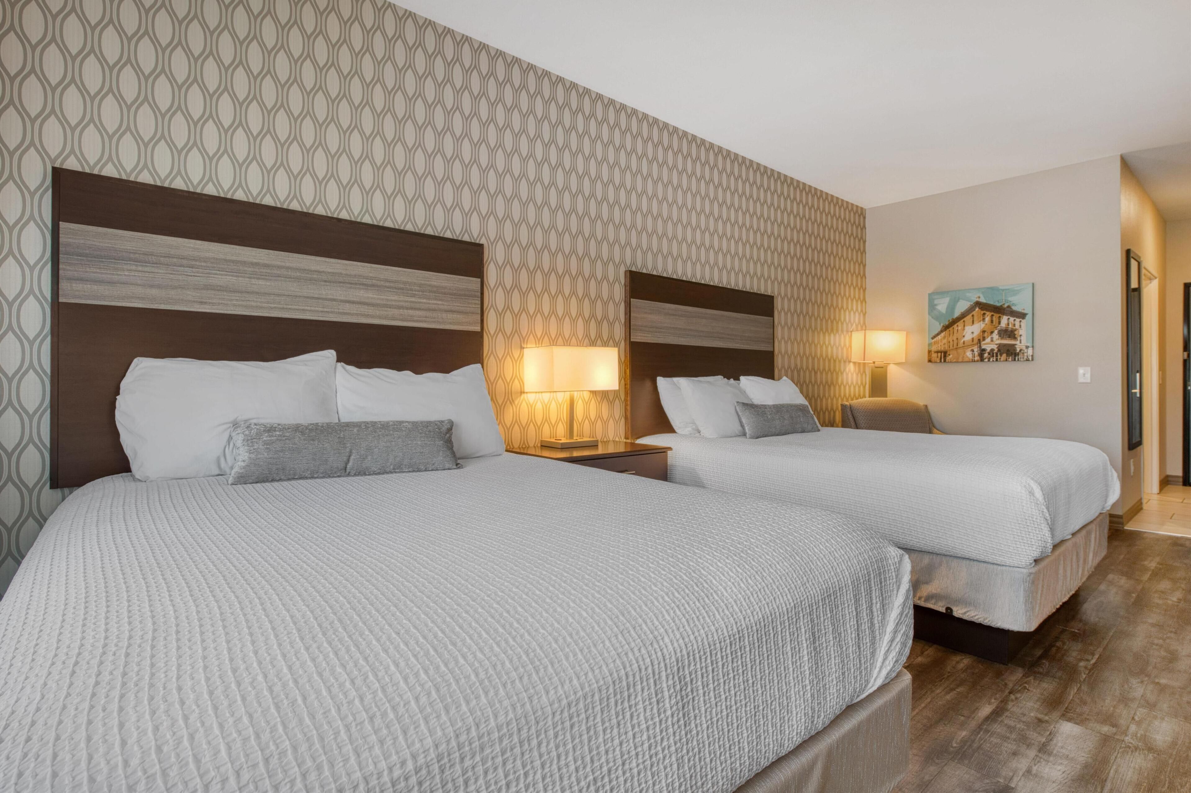A hotel room with two beds, patterned wallpaper, and a painting on the wall.