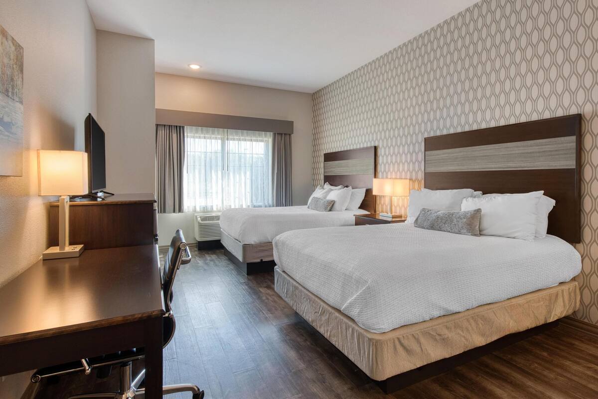 A hotel room with two beds, a desk, and a chair.