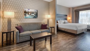 A hotel room with a patterned wallpaper, a large bed, a sofa, a coffee table, and two side tables with lamps. - Best Western Plus Saint Peter (Saint Peter)